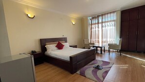 A hotel room with a bed, bedside tables, a desk, a chair, and a wardrobe. - Filimon Guest House (Addis Ababa)