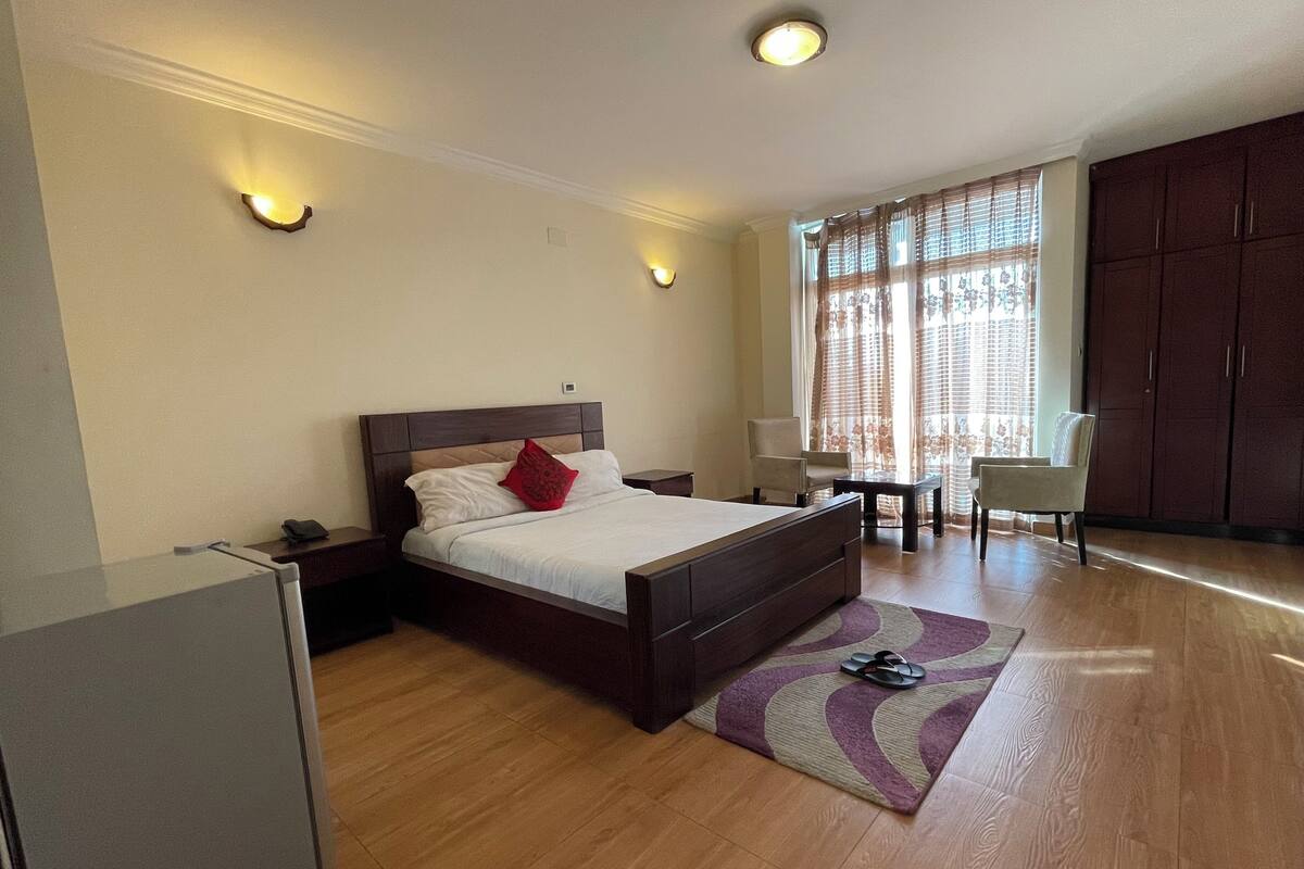 A hotel room with a bed, bedside tables, a desk, a chair, and a wardrobe.