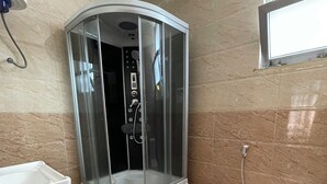 A bathroom with a glass-enclosed shower, a white sink, a toilet, and a window. - Filimon Guest House (Addis Ababa)