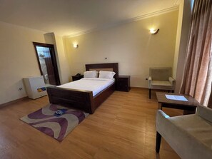 A hotel room with a bed, bedside tables, a chair, a desk, and a small refrigerator. - Filimon Guest House (Addis Ababa)