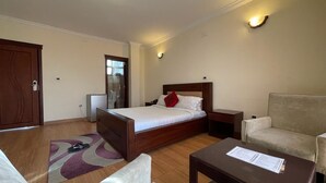 A hotel room with a bed, a sofa, a small table, and a chair. There is a door and a window in the room. - Filimon Guest House (Addis Ababa)