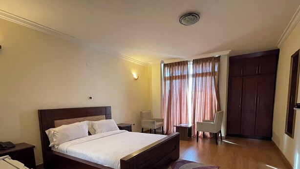 A hotel room with a wooden bed, a desk, a chair, a wardrobe, and a window with curtains. - Filimon Guest House (Addis Ababa)