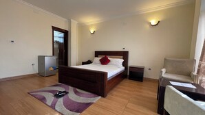 A hotel room with a wooden bed, a small bedside table, a chair, a desk, a rug, and a refrigerator. - Filimon Guest House (Addis Ababa)