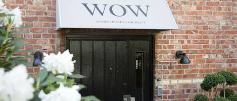 A brick building with a black door and a sign above it that reads "WOW APARTMENTS FOR RENT".