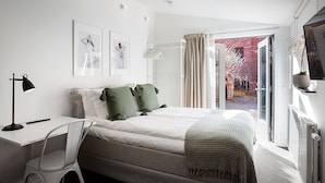 A modern bedroom with a bed, a desk, and a chair. There are two framed pictures on the wall, a window with curtains, and a view of the outside. - WOW Apartments & Rooms (Gothenburg)