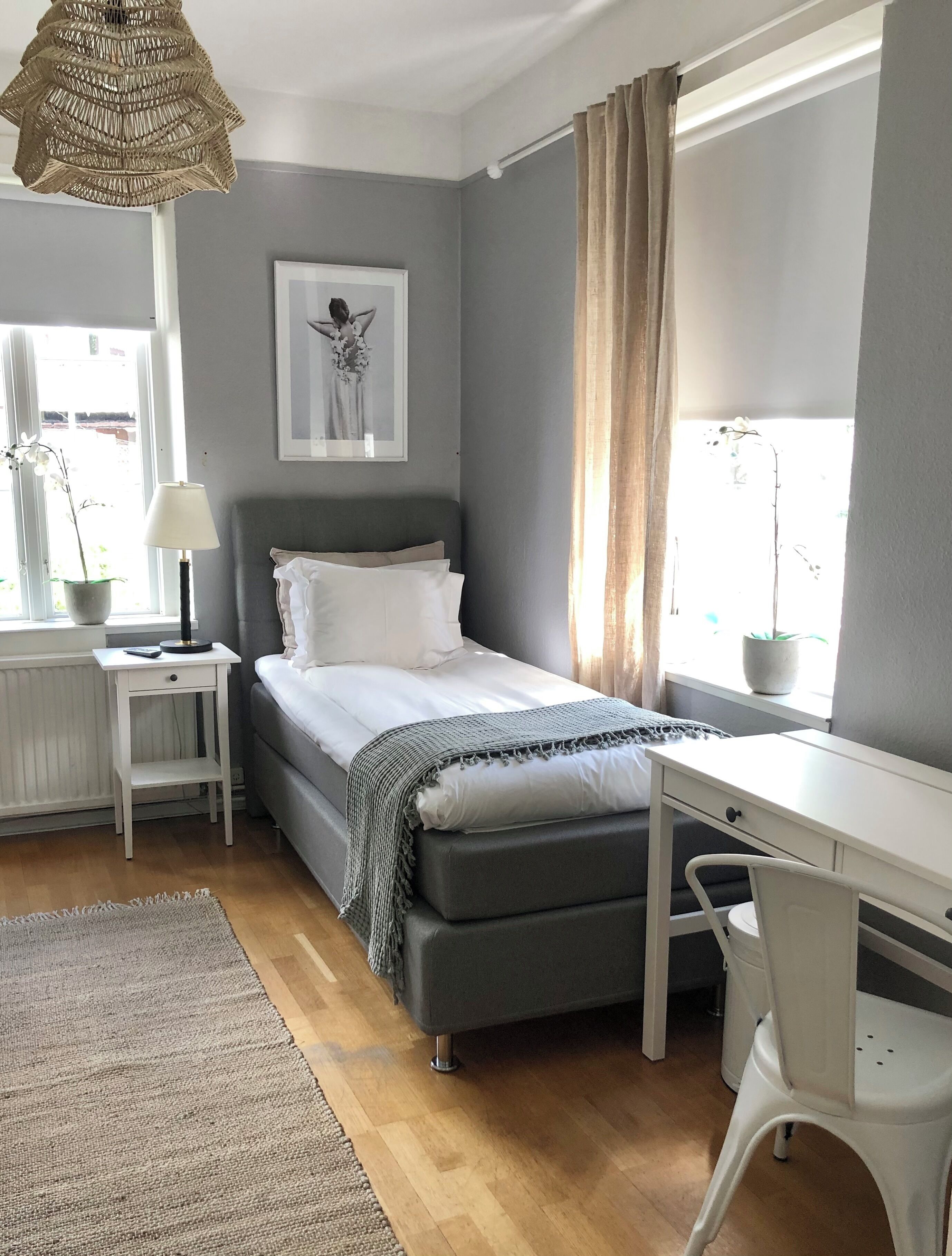 A bedroom with a bed, bedside table, lamp, desk, chair, and a window with curtains.