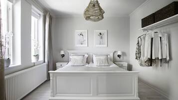 A bedroom with a large bed, two bedside tables, a hanging light fixture, and a window with curtains.