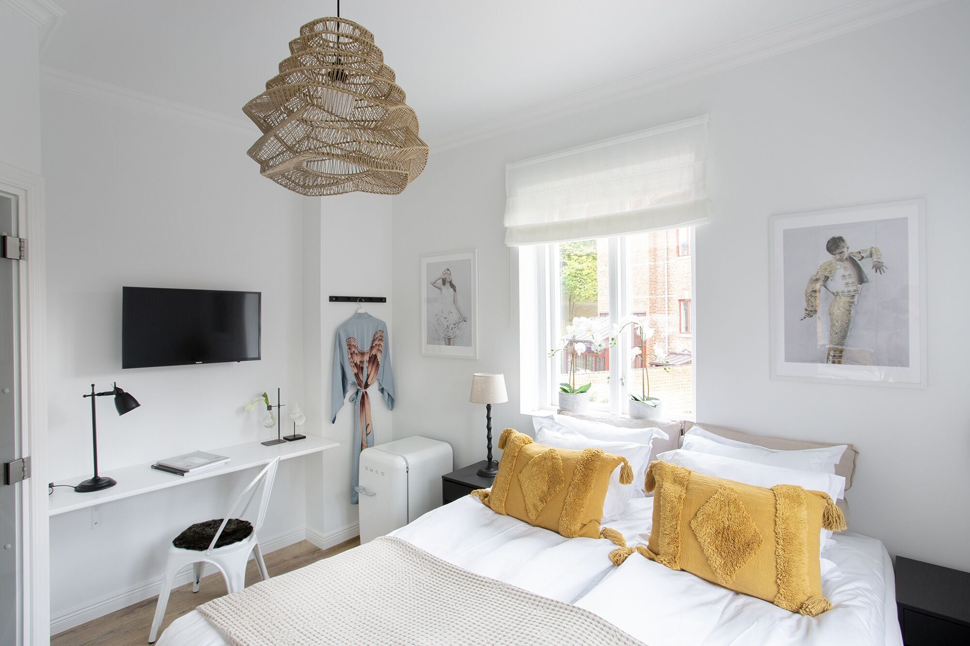Quarto de hotel com cama, escrivaninha, televisão e obras de arte nas paredes.