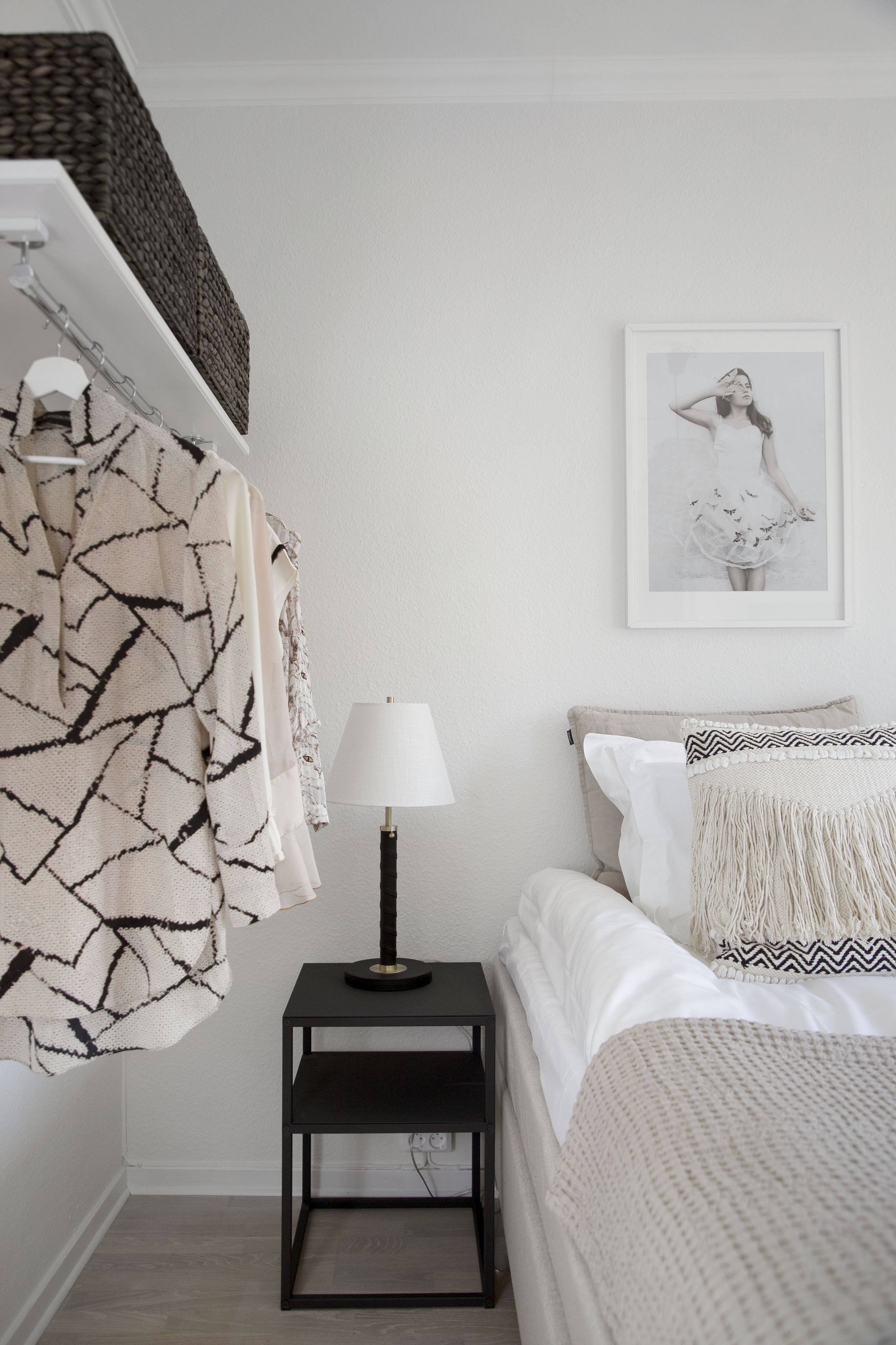 A bedroom with a bed, a bedside table with a lamp, a framed picture on the wall, and a hanging towel.