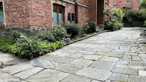 A stone-paved pathway leading to a red brick building with a number '7' sign, surrounded by greenery and a small entrance. - WOW Apartments & Rooms (Gothenburg)