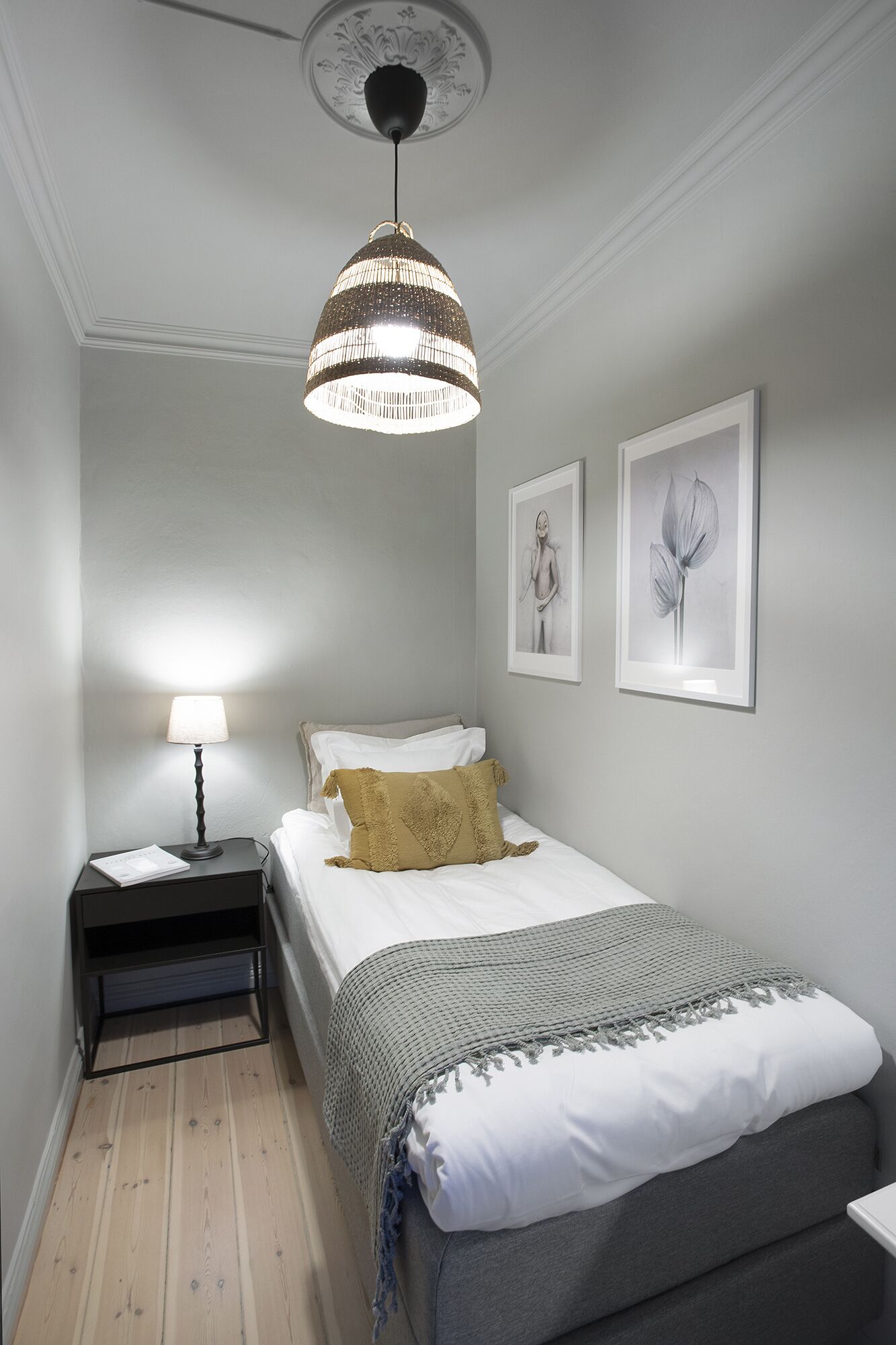 A bedroom with a bed, a nightstand, a lamp, a hanging light fixture, and two framed pictures on the wall.