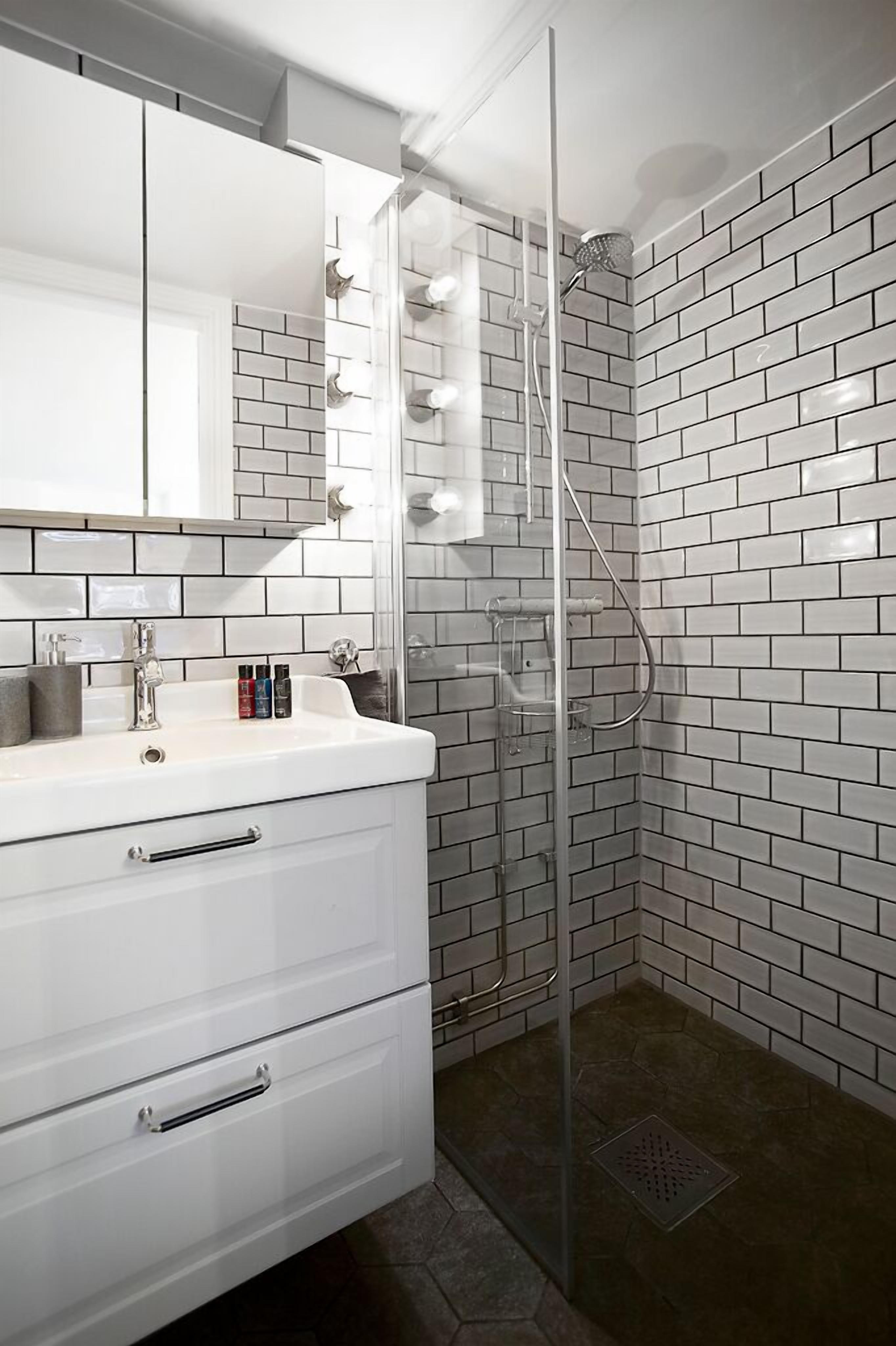 A bathroom with a white tiled shower, a glass-enclosed shower area, and a white vanity with a mirror and a sink.