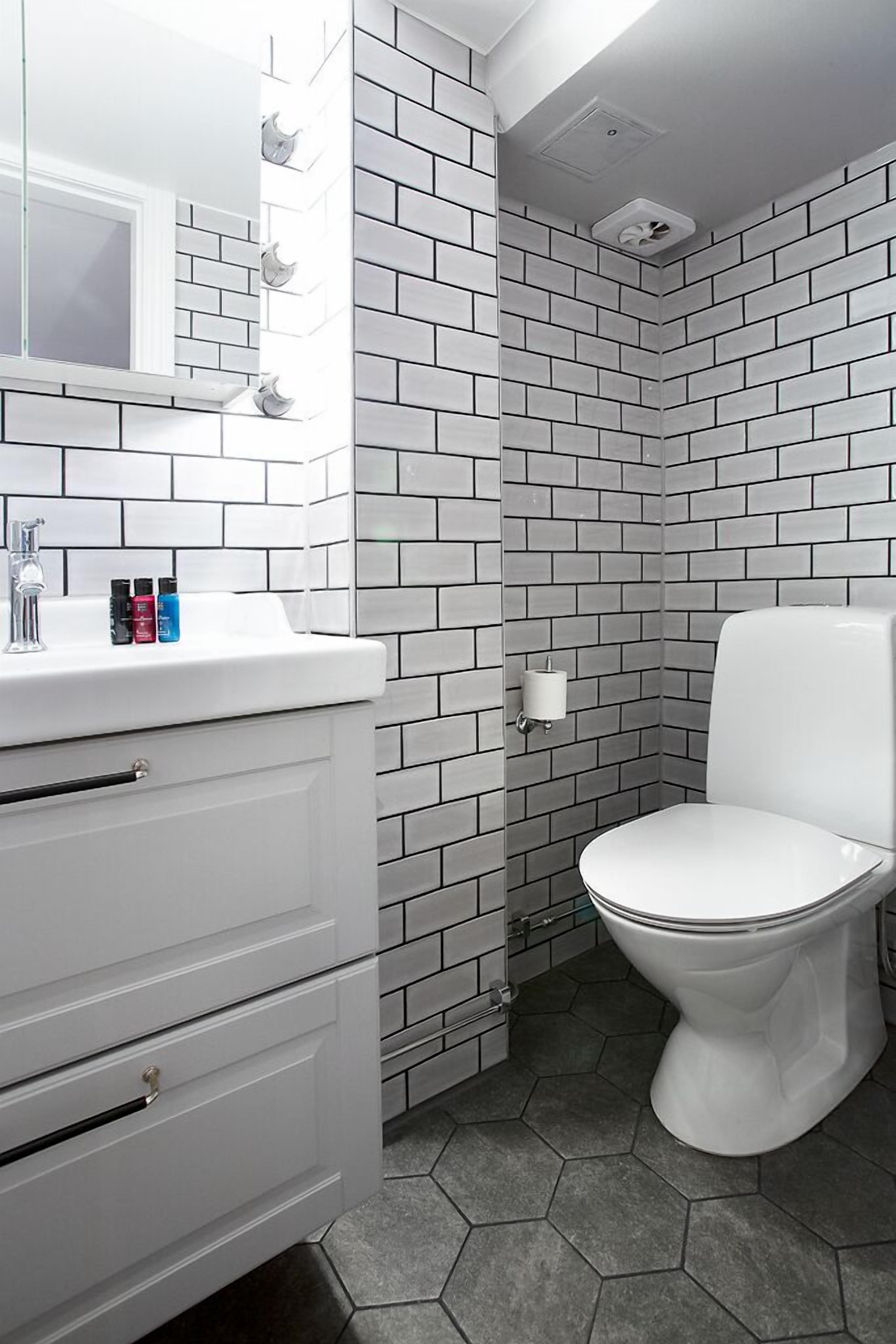 A bathroom with white subway tiles, a white toilet, a white sink with a mirror, and a white cabinet.