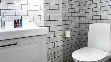 A bathroom with white subway tiles, a white toilet, a white sink with a mirror, and a white cabinet.