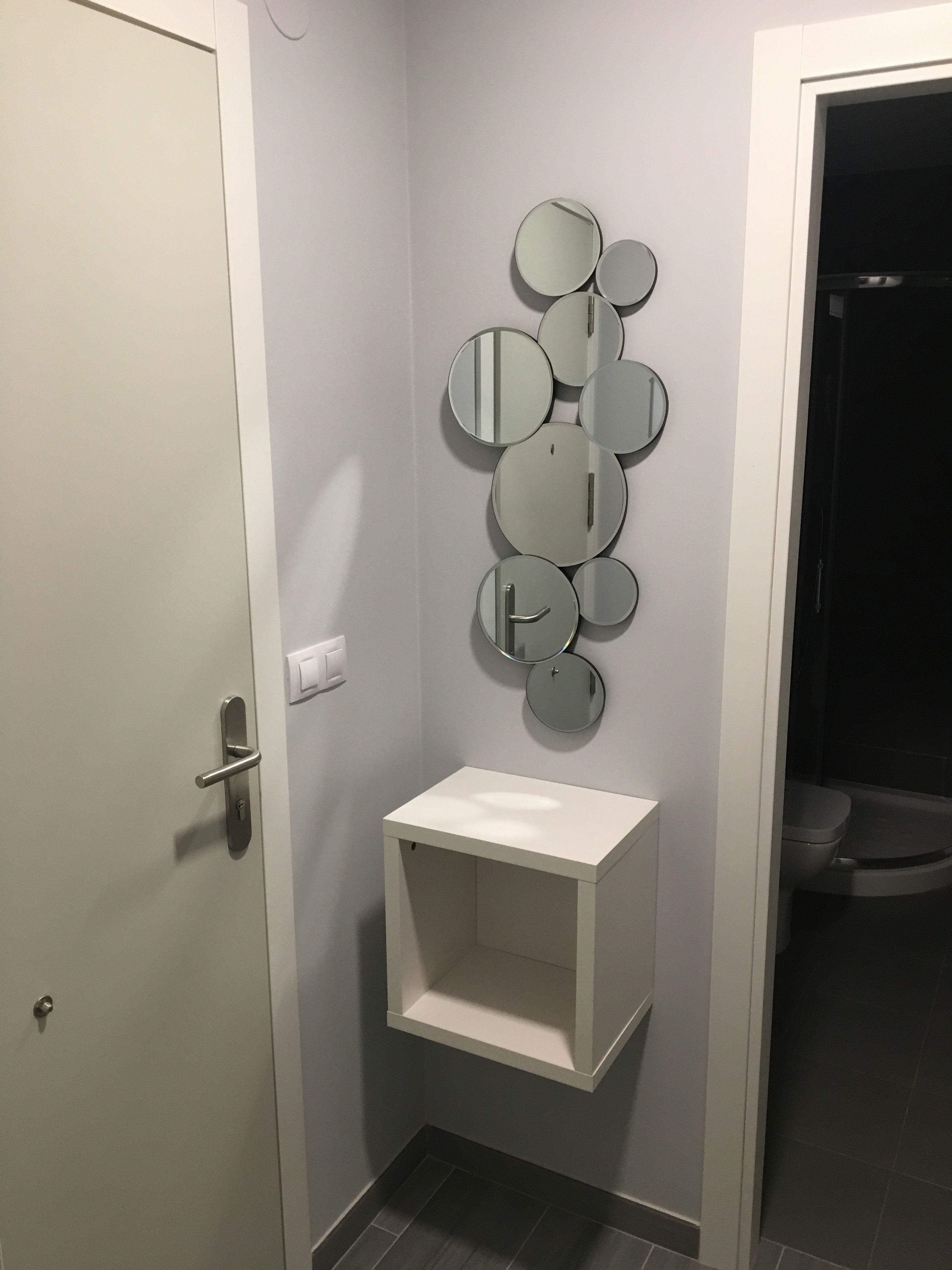 Un bany amb una porta blanca, un lavabo blanc amb un mirall a la part superior i un vàter visible a la sala adjacent.