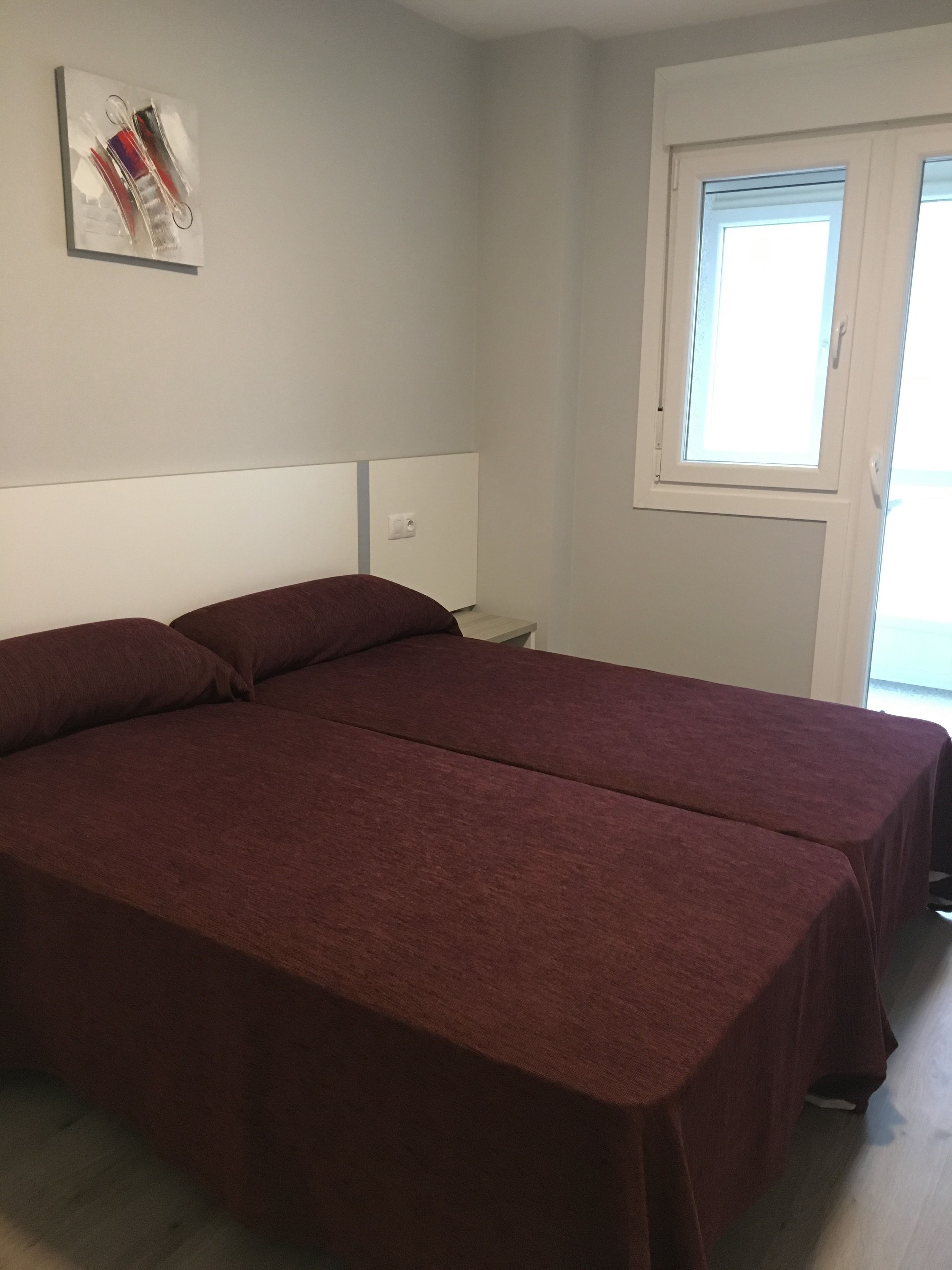Une chambre avec deux lits simples, une petite table de chevet, une commode, une fenêtre avec des stores et une œuvre d’art accrochée au mur.