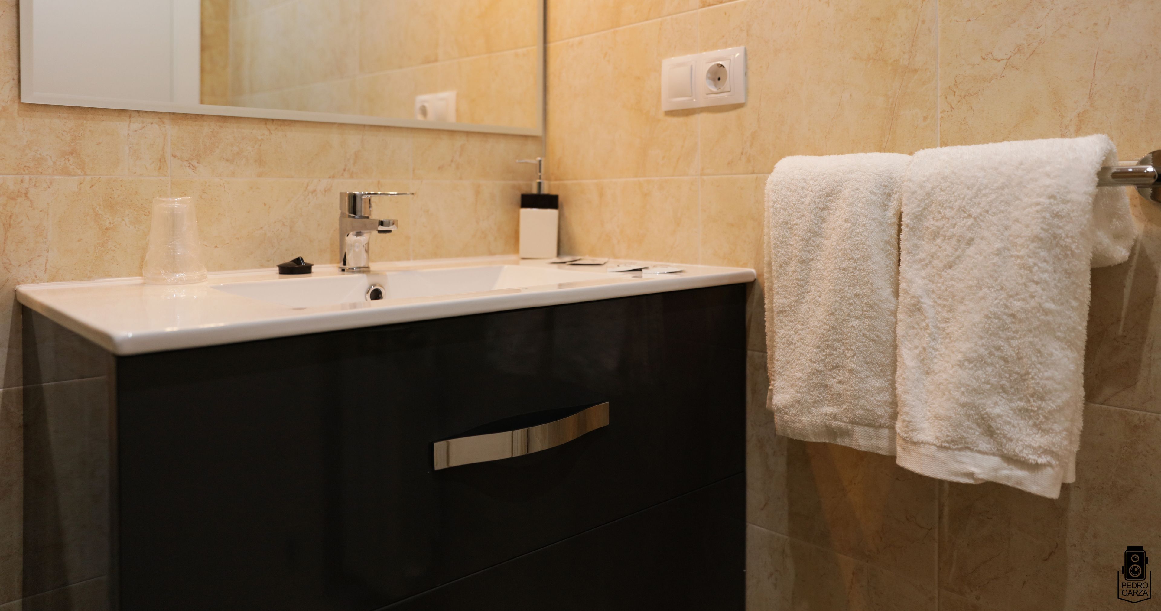 A modern bathroom with a white sink, dark cabinets, and a towel rack with two white towels.