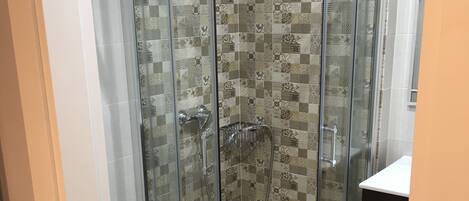 Une cabine de douche fermée par des parois en verre, avec un mur recouvert de carreaux, des toilettes blanches et un meuble noir.