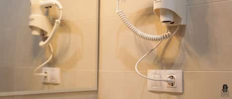 A hairdryer mounted on a wall with a power outlet below it.