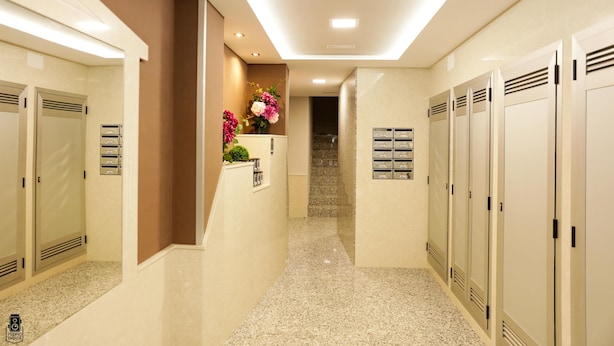 Pasillo de hotel con taquillas, mostrador de recepción y escalera que sube a un piso superior.