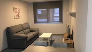 Un espacio habitable pequeño y moderno con un sofá gris, una mesa blanca y un televisor pequeño.
