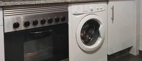 Una cocina con estufa de acero inoxidable, horno integrado, lavadora y armarios blancos.
