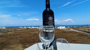 A bottle of Nemea wine and a glass on a table with a view of a coastal landscape. - Santo Margarita (Santorini)