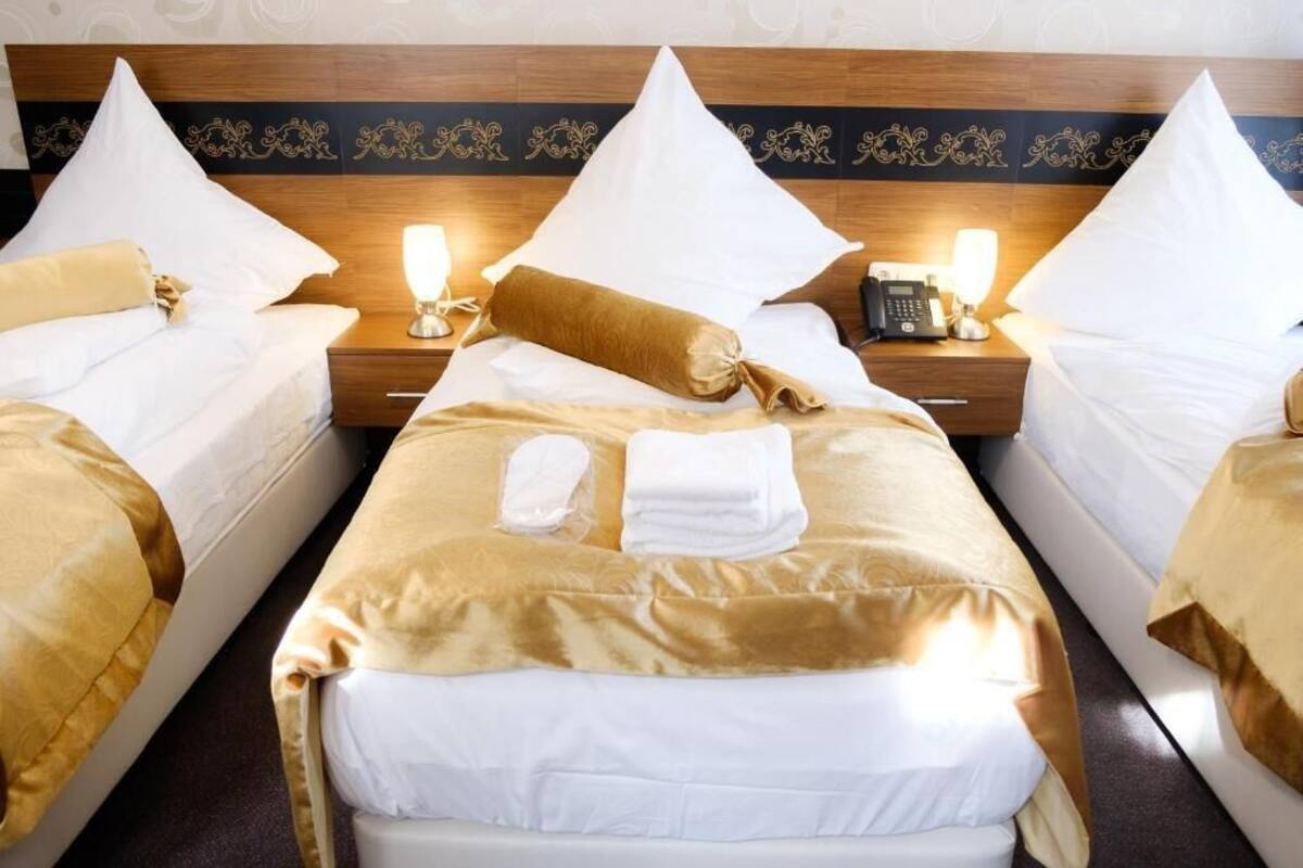A hotel room with two beds, each with a headboard, white bedding, and a golden accent pillow. There are bedside lamps and a telephone on the nightstand.