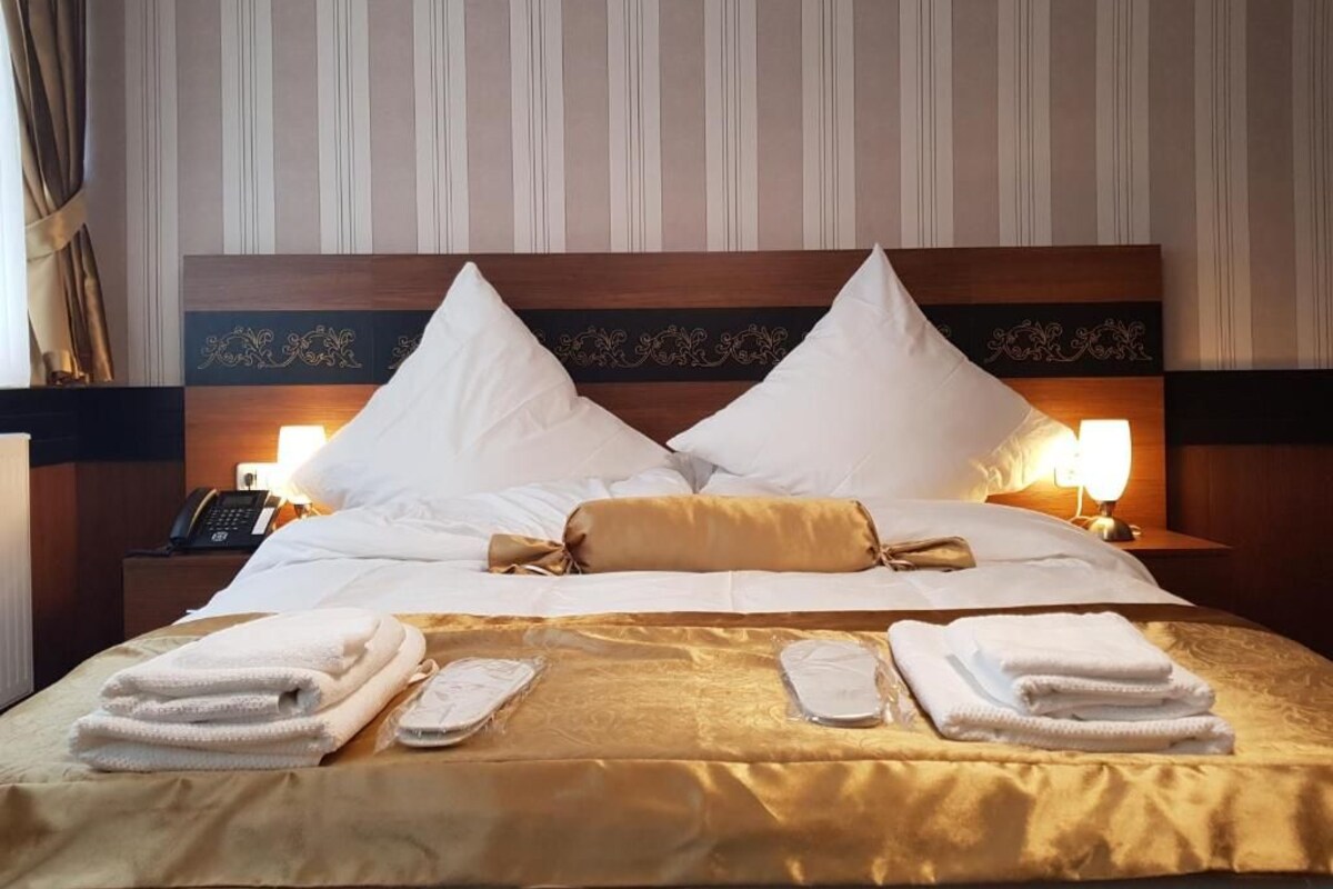 A hotel room with a large bed, two bedside lamps, a telephone on the nightstand, and neatly folded towels.