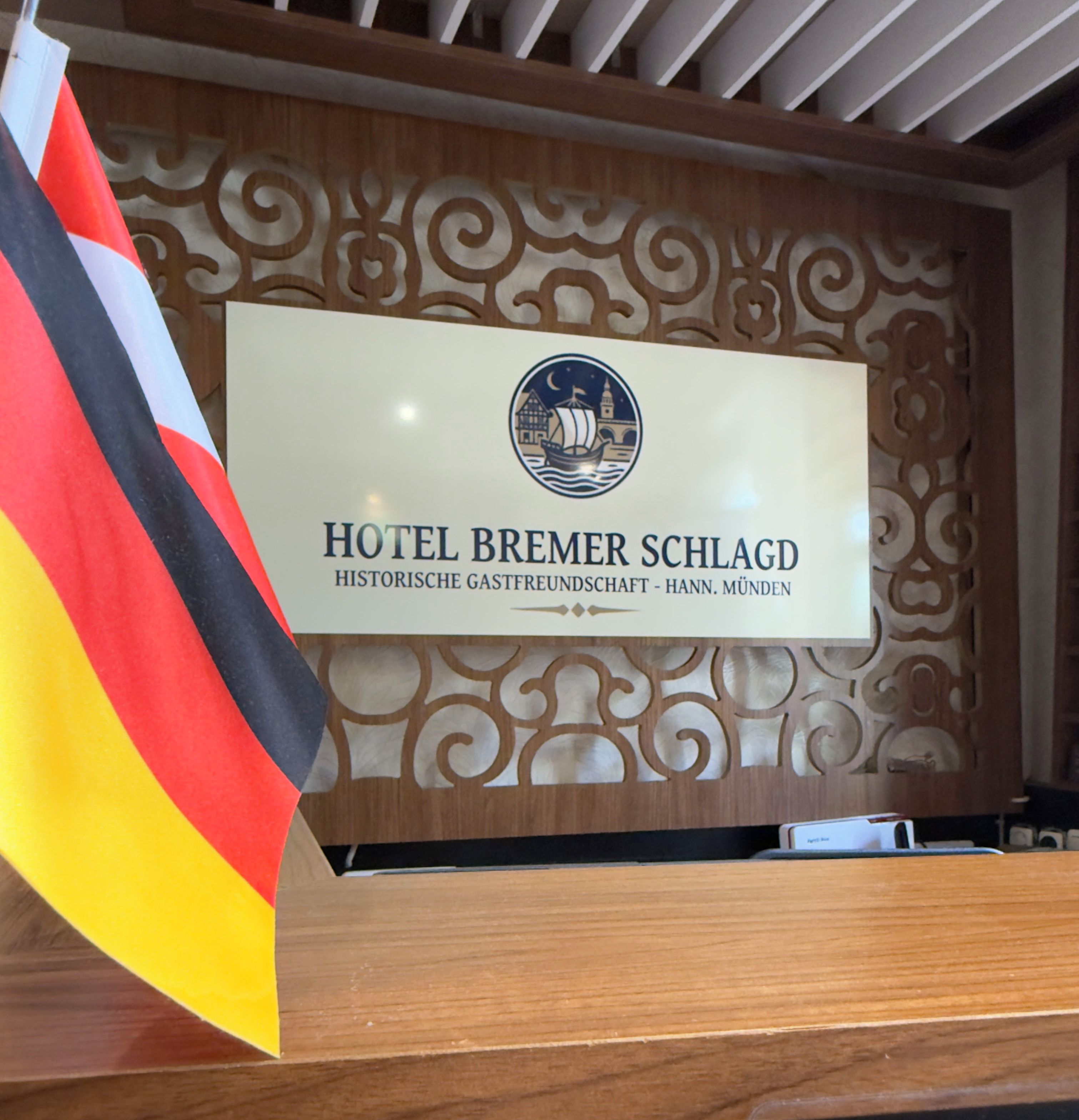 Una recepción de hotel con un cartel que muestra el nombre 'HOTEL BREMER SCHLAGD' y una bandera.