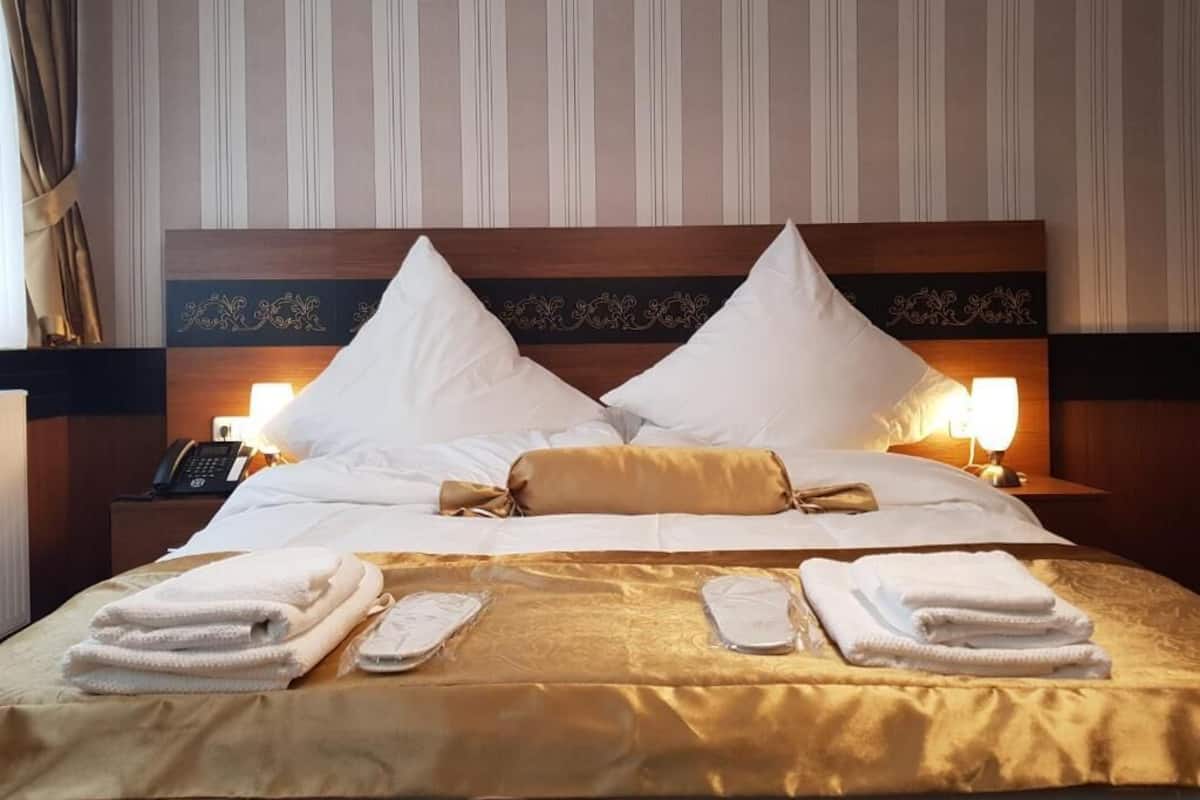 A hotel room with a large bed, two bedside lamps, a telephone on the nightstand, and neatly folded towels.