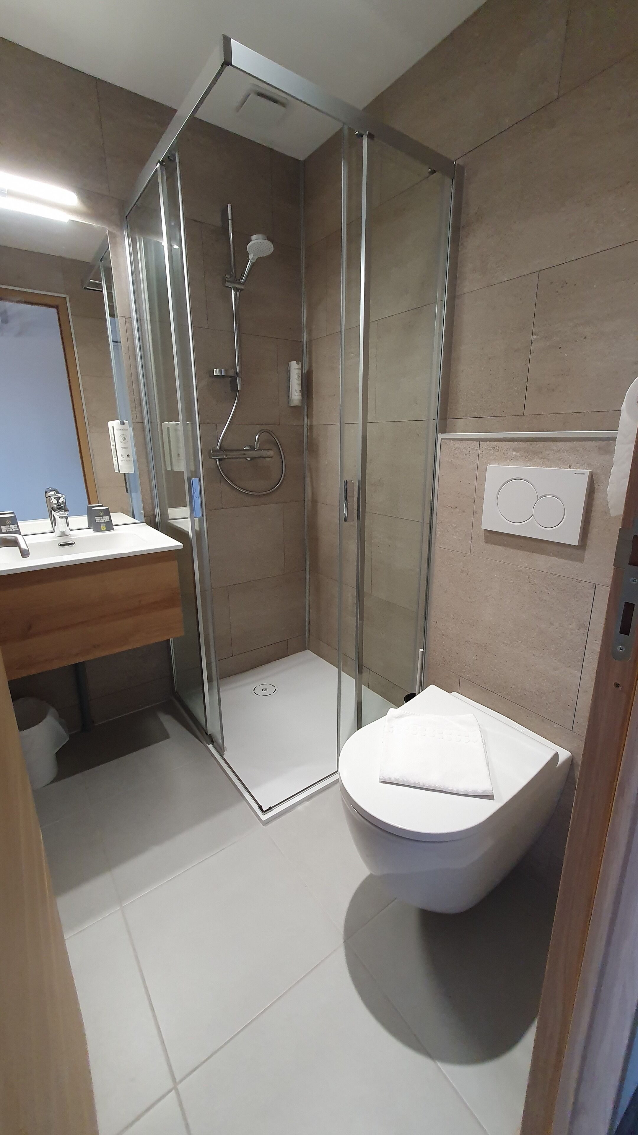 Une salle de bain moderne avec une douche à parois de verre, des toilettes blanches et un lavabo avec un miroir.
