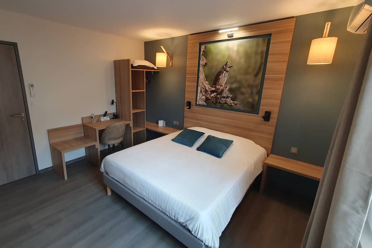 A hotel room with a bed, desk, chair, and a painting on the wall.