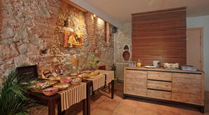 A rustic kitchen with a stone wall, wooden counter, and a dining area with a striped tablecloth. - Hotel Les Pasteliers (Lavaur)