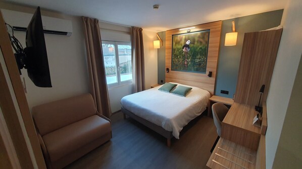 A hotel room with a bed, a seating area, a desk, and a painting on the wall. - Hotel Les Pasteliers (Lavaur)