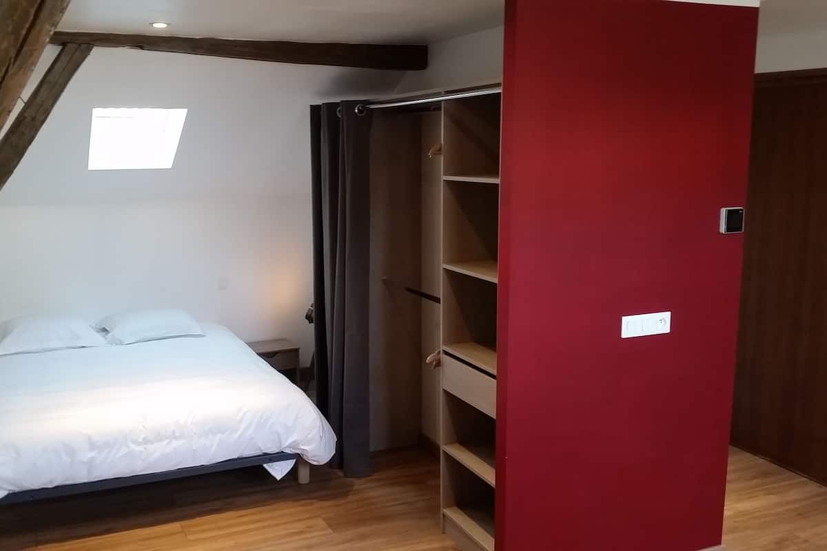 A bedroom with a bed, a red wardrobe, and a small window.