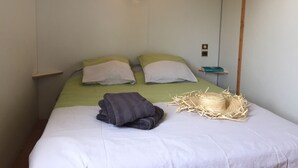 A neatly made bed with green and white bedding, a folded grey towel, and a straw hat on the bed. - Camping des Platanes (Charny-Oree-de-Puisaye)
