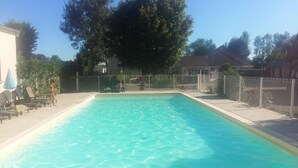 A rectangular swimming pool with a clear blue water surface, surrounded by a fence and trees. - Camping des Platanes (Charny-Oree-de-Puisaye)