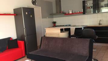 A compact living space with a kitchenette, a red sofa, a black couch, and a dining table.