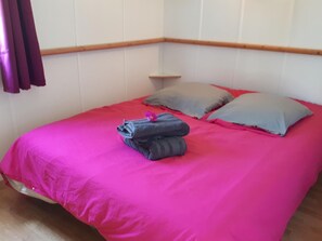 A room with a bed, pillows, and a folded towel on the bed. - Camping des Platanes (Charny-Oree-de-Puisaye)
