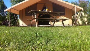 A tent with a picnic table in front, set in a grassy area with trees in the background. - Camping des Platanes (Charny-Oree-de-Puisaye)