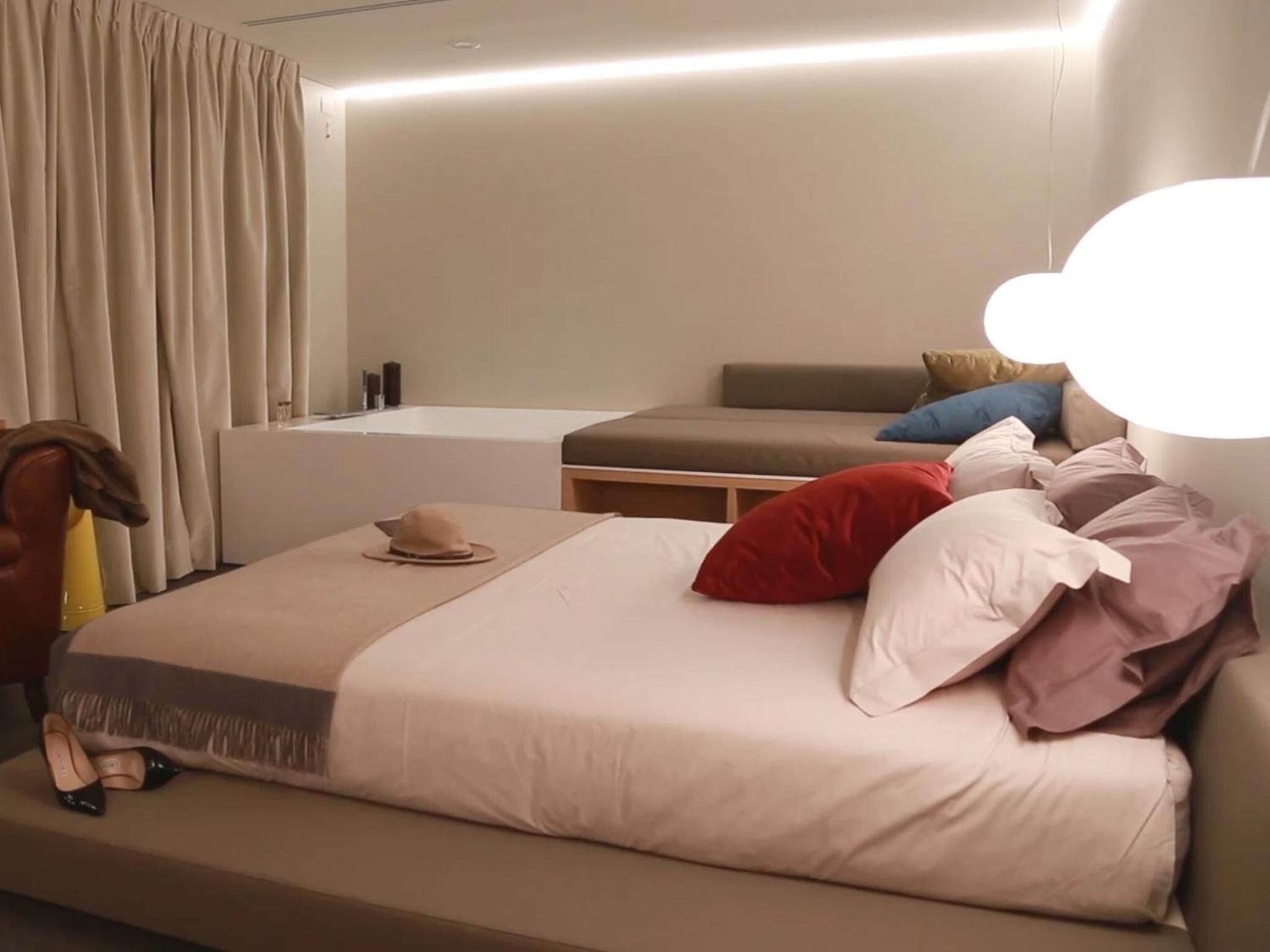 A modern hotel room with a large bed, a small sofa, and a bathroom with a bathtub.
