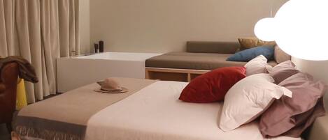 A modern hotel room with a large bed, a small sofa, and a bathroom with a bathtub.