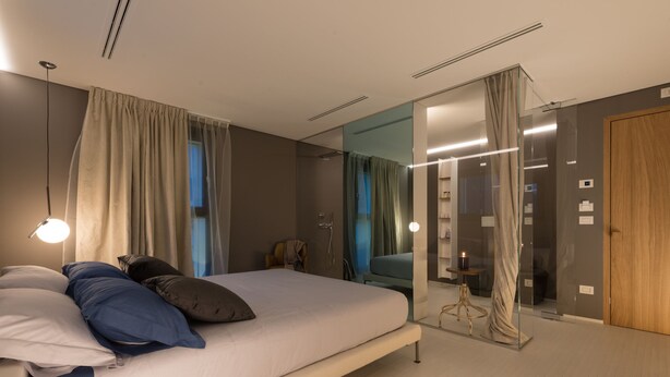 Un dormitorio moderno con una cama grande, un divisor de ambiente de vidrio y una puerta de madera.