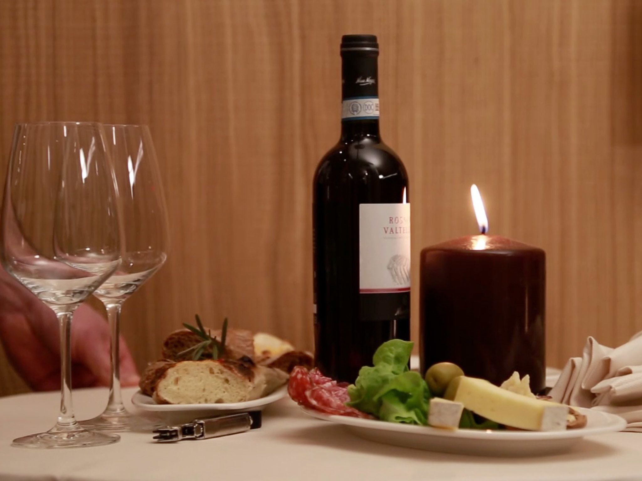 Una mesa con una botella de vino, dos copas, una vela encendida y un plato de comida.