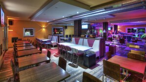 Un restaurante con varias mesas y sillas, una zona de bar y una pantalla de televisión.