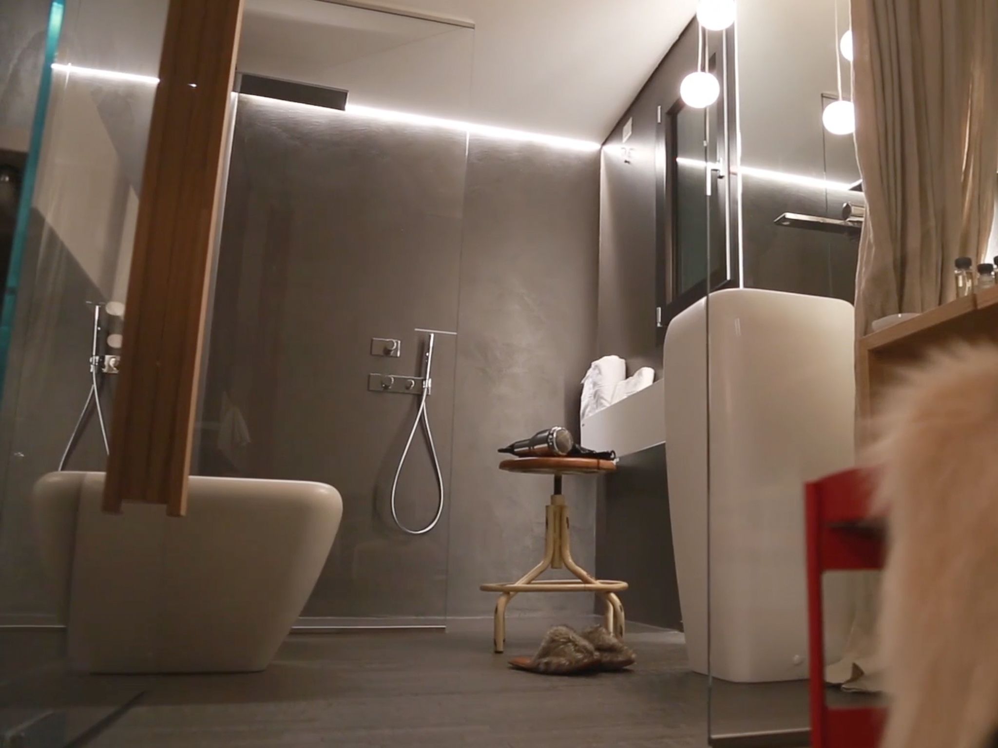 A modern bathroom with a glass shower enclosure, a white bathtub, and a small vanity with a mirror.