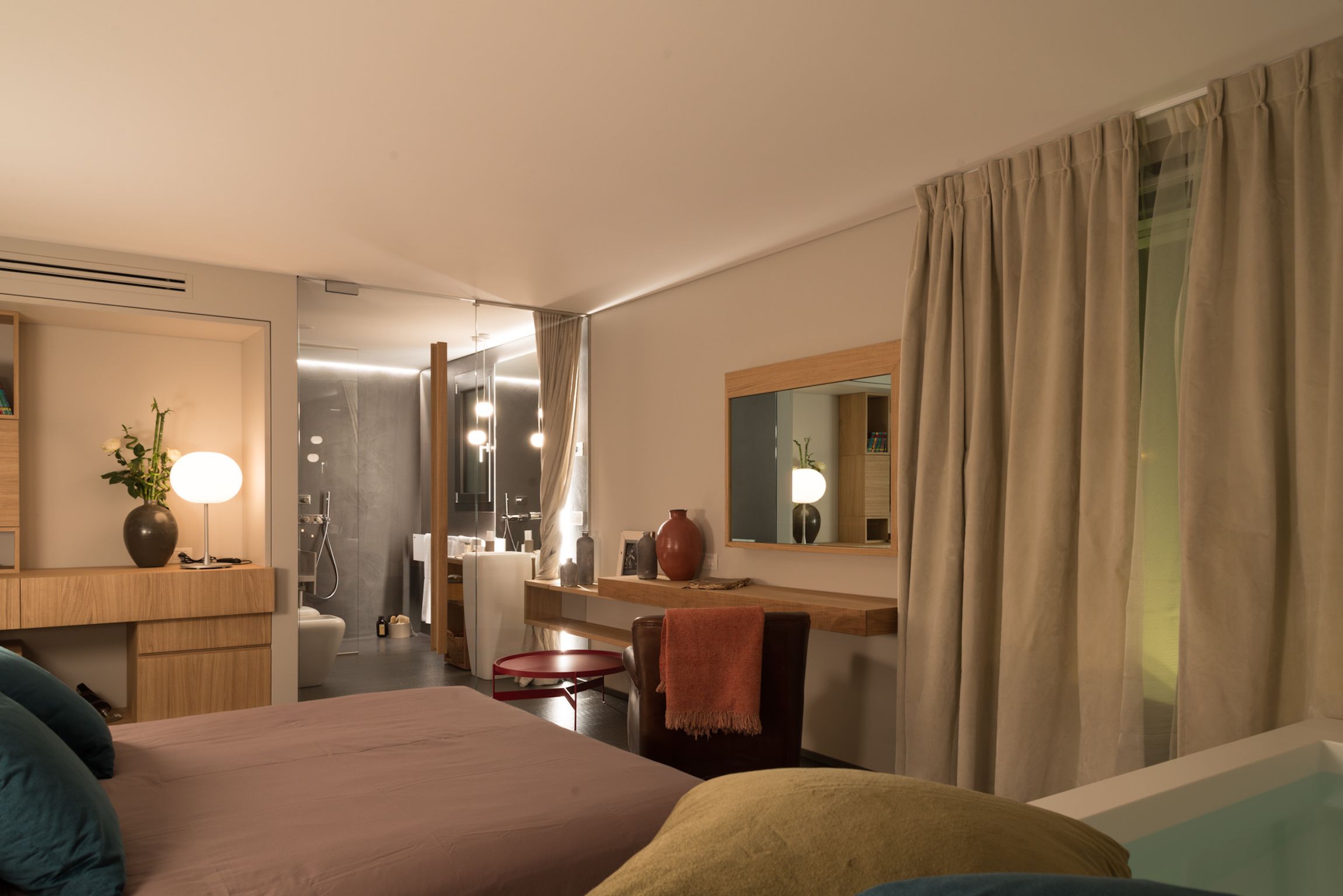 Una habitación de hotel moderna con una cama grande, un escritorio, un espejo y un baño visible a través de una puerta abierta.
