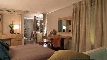 Una habitación de hotel moderna con una cama grande, un escritorio, un espejo y un baño visible a través de una puerta abierta.