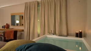 Habitación de hotel con bañera, espejo, ventana con cortinas y dos velas a un lado.